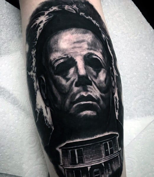 Bold black and gray Michael Myers tattoo featuring his menacing mask with the eerie Myers house below, enhancing the horror vibe.