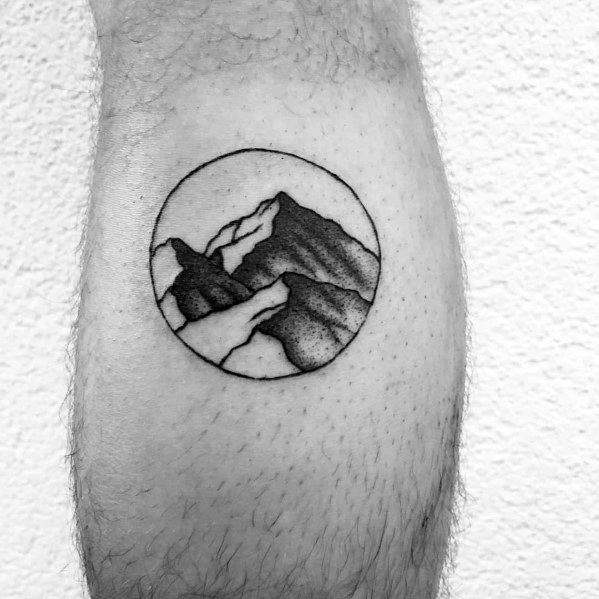 Minimalist circular mountain tattoo on the leg, featuring fine lines and soft shading for a clean and nature-inspired landscape design.