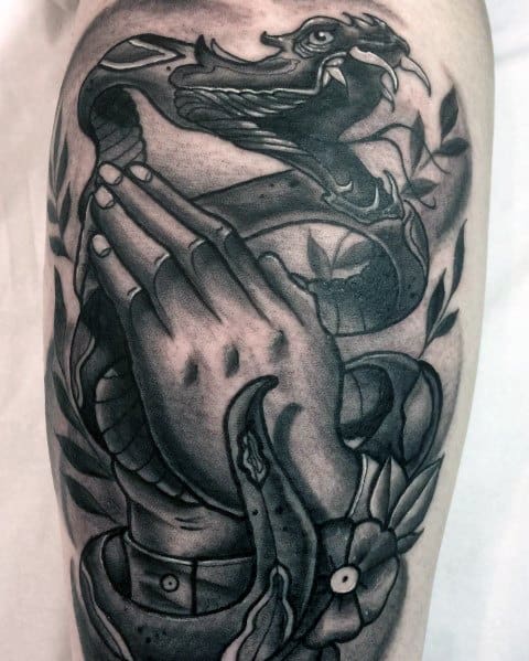 Neo-traditional black and grey tattoo of praying hands with a fierce snake coiled around them, featuring bold shading and intricate detailing.