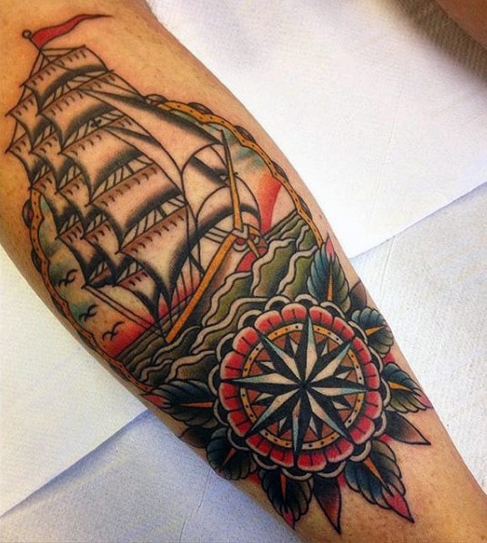 Traditional-style calf tattoo of a sailing ship on rough waters, framed by a bold compass rose and floral details in vibrant colors