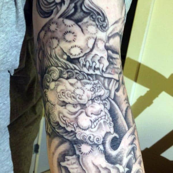 Black and grey tattoo of a traditional Chinese guardian lion (Foo Dog), featuring intricate shading and swirling patterns for a bold design
