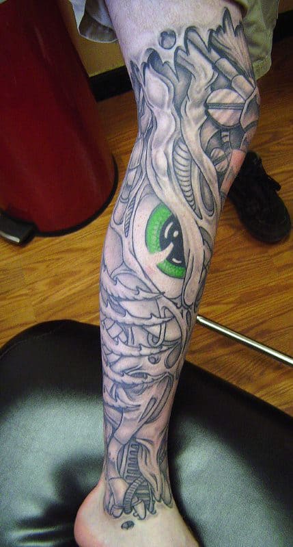 Tattoo of a stylized eye with surrounding abstract shapes covering a lower leg