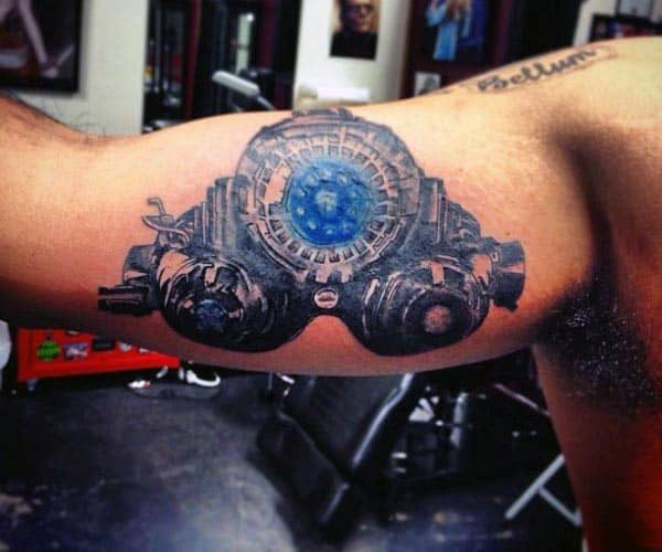 Futuristic black and grey tattoo of a high-tech mechanical device with a glowing blue core, resembling a cyberpunk or sci-fi theme on the bicep