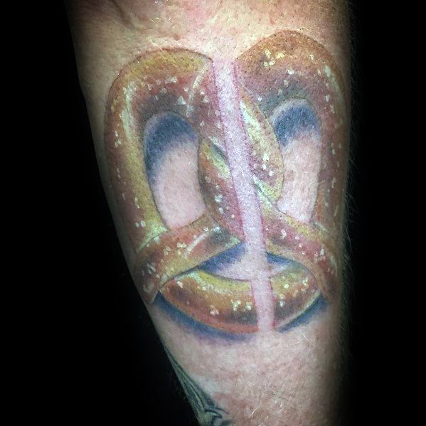 Realistic pretzel tattoo with detailed shading, salt specks, and a bold three-dimensional effect, placed on the forearm.