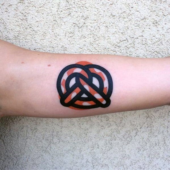 Bold black and orange pretzel tattoo with a geometric design, featuring thick outlines and a modern, minimalist aesthetic on the forearm.