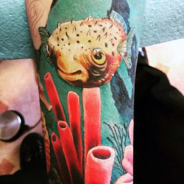 Realistic pufferfish tattoo with intricate shading, vibrant coral reef background, and lifelike details, creating an immersive underwater scene.
