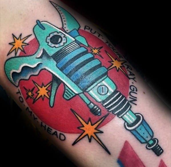 Bold and colorful ray gun tattoo with a futuristic sci-fi design, featuring blue and teal tones, explosive accents, and a striking red background.