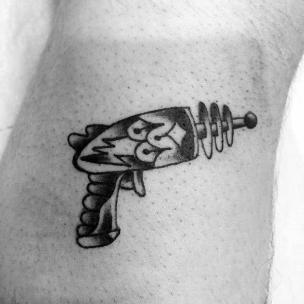 Small black and grey ray gun tattoo with a retro sci-fi design, featuring bold shading, lightning details, and a classic coil barrel for a vintage look.