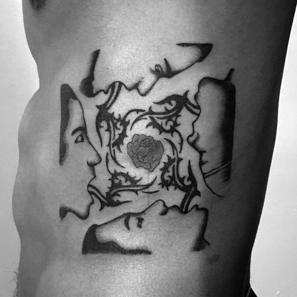 Side torso tattoo inspired by the *Blood Sugar Sex Magik* album cover, featuring four faces around an ornate floral design in black ink.