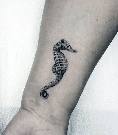 Minimalist black and grey seahorse tattoo on wrist, featuring fine details and subtle shading for a delicate and elegant marine-inspired design.