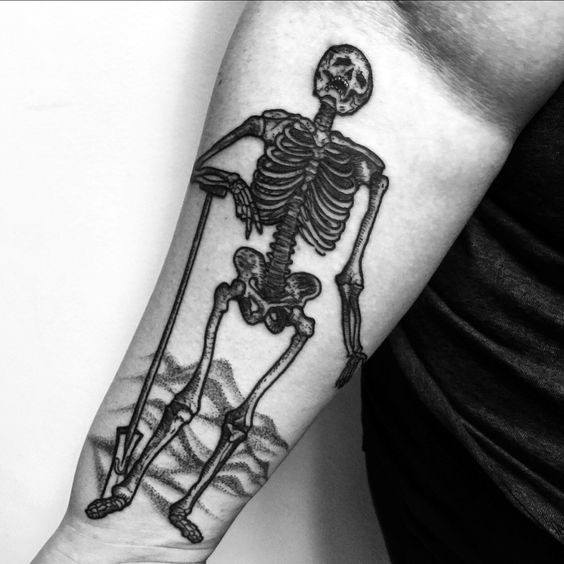 Black and grey tattoo of a skeleton leaning on a shovel, standing over a freshly dug grave, symbolizing mortality, time, and the cycle of life.