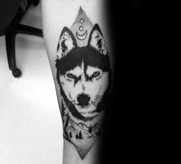 Blackwork Siberian Husky tattoo on a man's leg, featuring bold lines, dot work shading, a forest scene, and celestial elements for a mystical design.