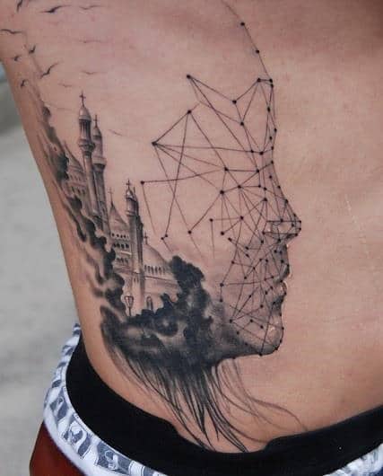 A tattoo of a castle and geometric face outline on a person's side torso