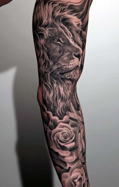 Full-sleeve tattoo of a realistic lion's face with detailed floral designs in grayscale