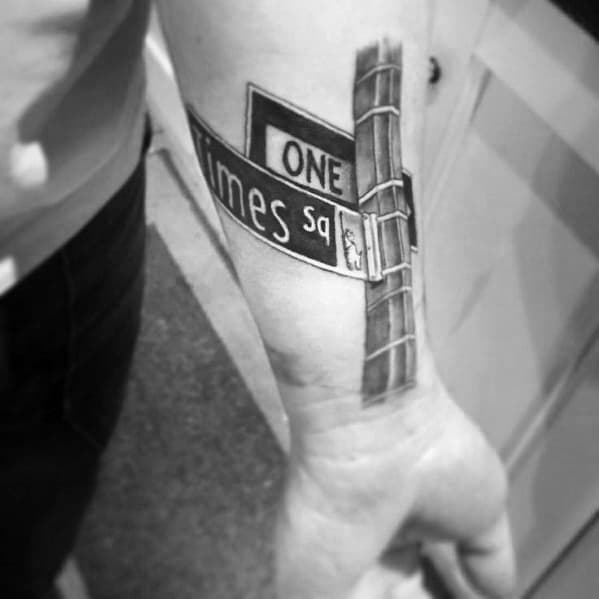 Black and grey tattoo of a detailed 'One Times Sq' street sign on the forearm, with realistic shading and bold lettering.
