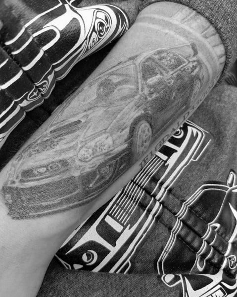 Realistic black and grey Subaru WRX STI tattoo on the forearm, featuring a detailed front view with shading for depth and a dynamic effect.