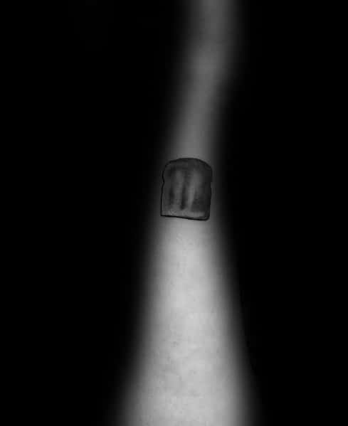 Tiny minimalist toast tattoo in black ink, featuring soft shading for a subtle and simple design on the forearm.