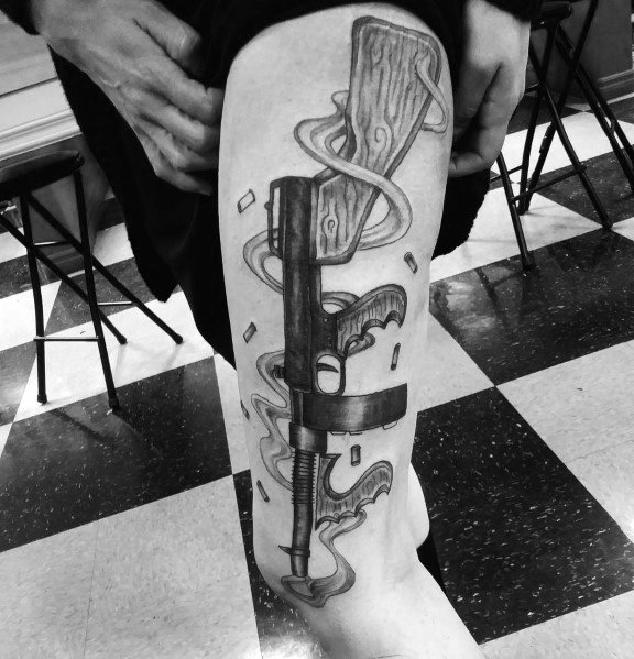 Black and grey Tommy gun tattoo on the thigh, featuring smoke, floating playing cards, and wood grain details for a bold and dynamic gangster aesthetic.