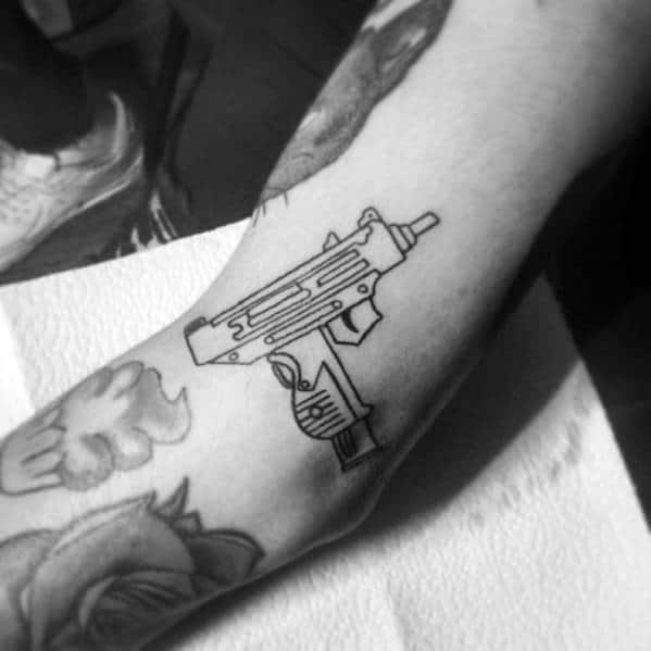 Minimalist black outline Uzi tattoo on the forearm with clean lines and a simple yet bold design, blending seamlessly with surrounding tattoos.