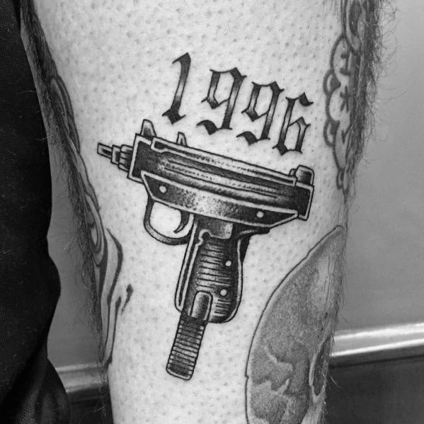 Black and grey Uzi tattoo on the leg with "1996" in bold gothic lettering above, featuring fine shading and a classic firearm design.