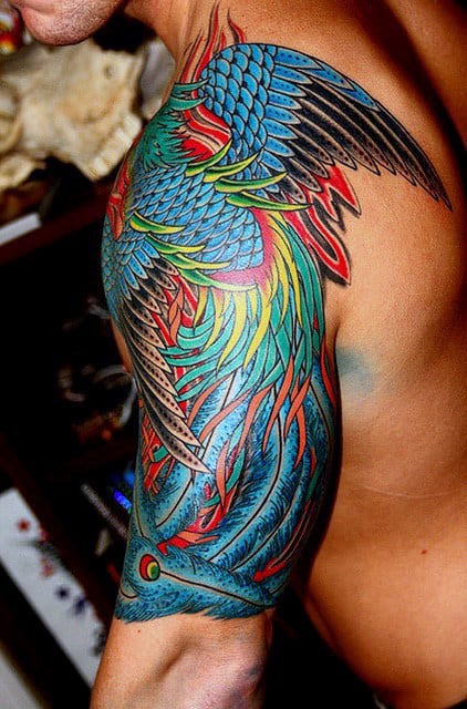 Colorful, intricate bird tattoo covering a person's shoulder and upper arm