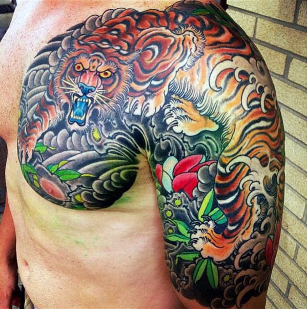 Man's chest and shoulder tattoo of a fierce tiger among colorful clouds and foliage