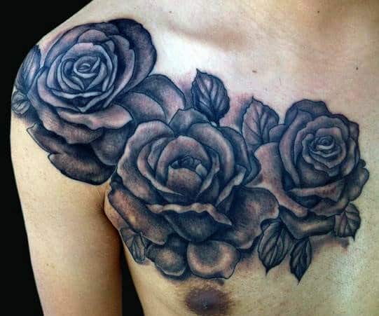 Black and gray rose tattoos elegantly bloom across a person's upper chest, seamlessly extending onto their shoulder