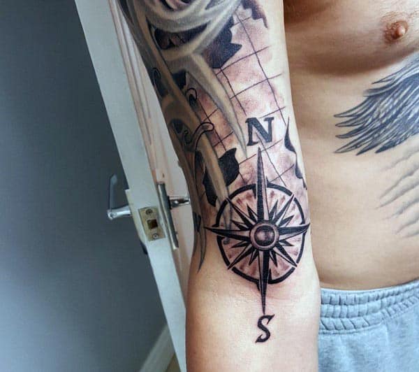 Black and grey tattoo of a detailed compass rose with a world map background, featuring bold lines and shading on the forearm