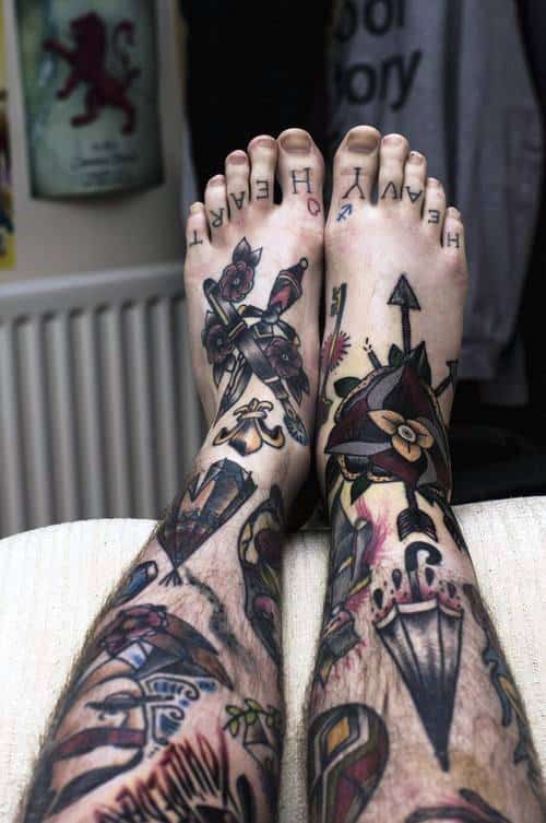 Tattooed legs and feet with various designs, letters on toes spell "HEAVY HEART