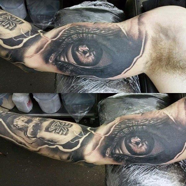 Black and grey realistic tattoo of a detailed eye with a reflection inside, surrounded by cracked skin effects and a skull design on the arm
