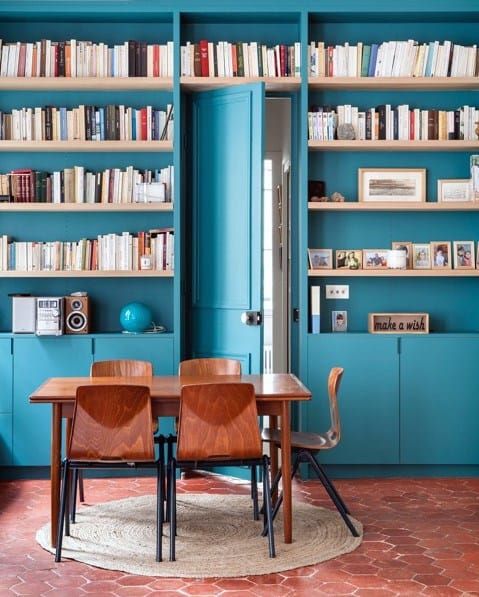 Cozy dining area with a turquoise bookshelf, wooden table, and chairs on a round rug