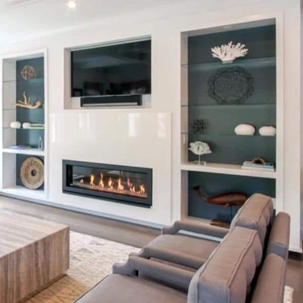 Contemporary family room with built-in bookcases featuring glass shelves, a sleek gas fireplace, and a mounted TV, accented by teal backing and modern decor