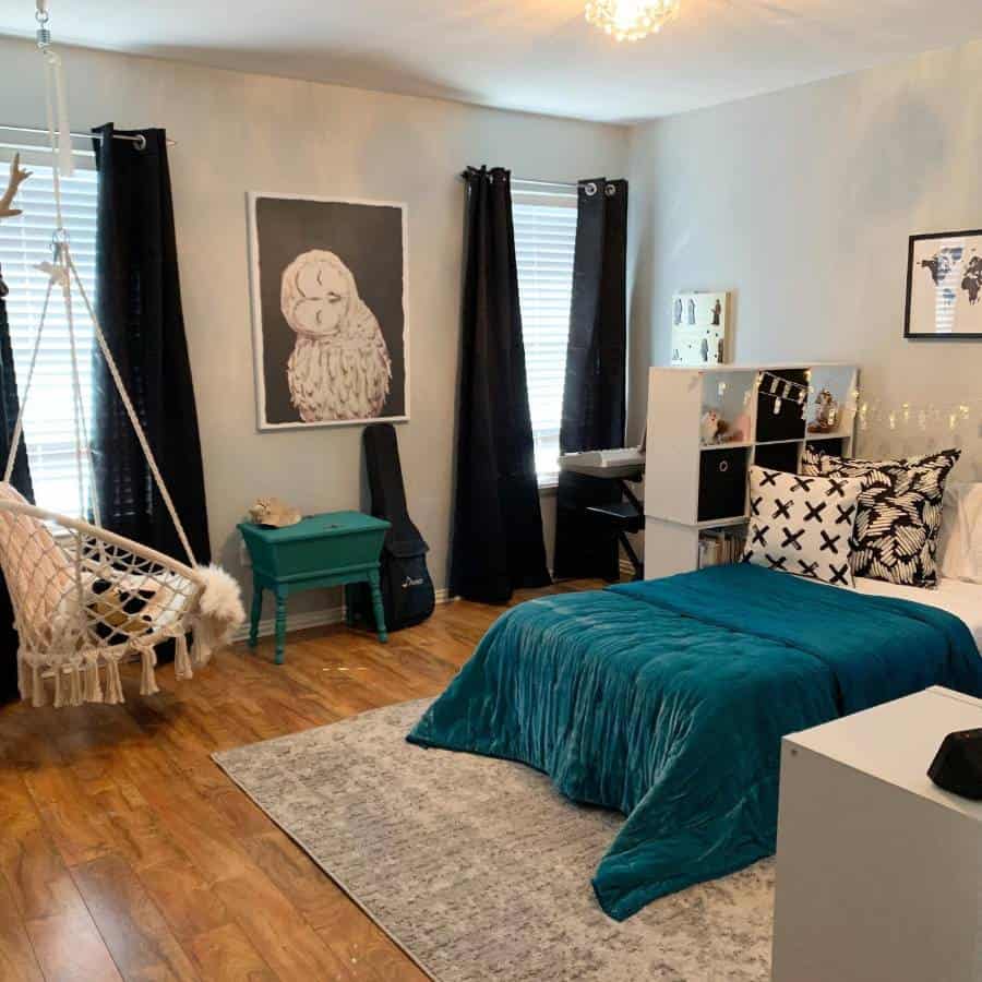 Cozy bedroom with teal bedding, owl wall art, hanging chair, and dark curtains.