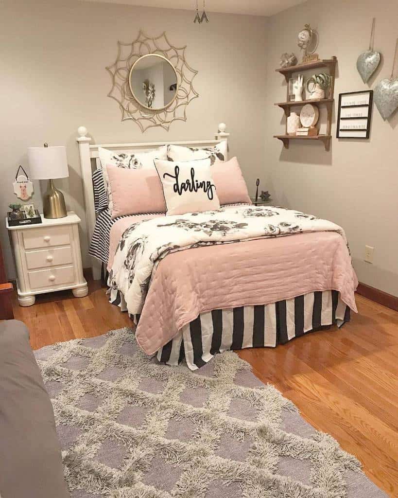Cozy farmhouse-style bedroom with pink bedding, mirror, shelves, and white nightstand.