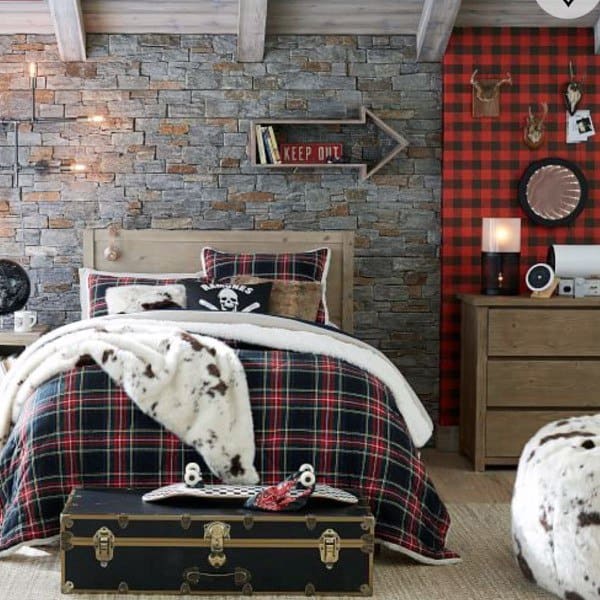 Cozy bedroom with plaid bedding, stone wall, and rustic decor, trunk at the foot of bed, arrow sign on wall