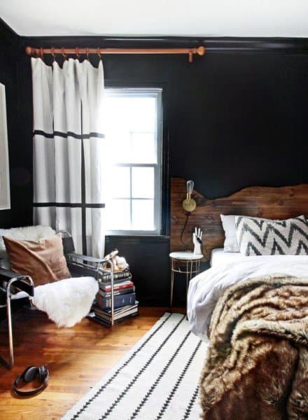 Cozy bedroom with dark walls, a large window, and stylish decor including a chair, books, and a zigzag pillow