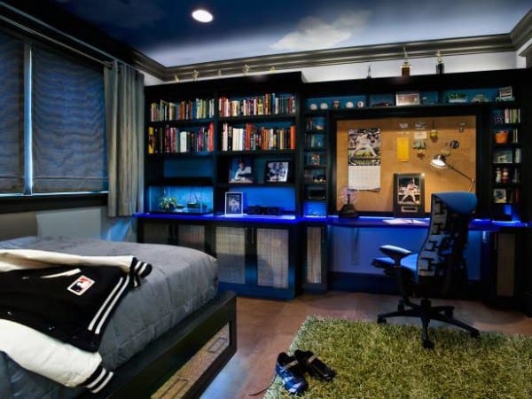 Room with a bed, bookshelves, corkboard, and gaming chair. Blue lighting highlights shelves and desk area