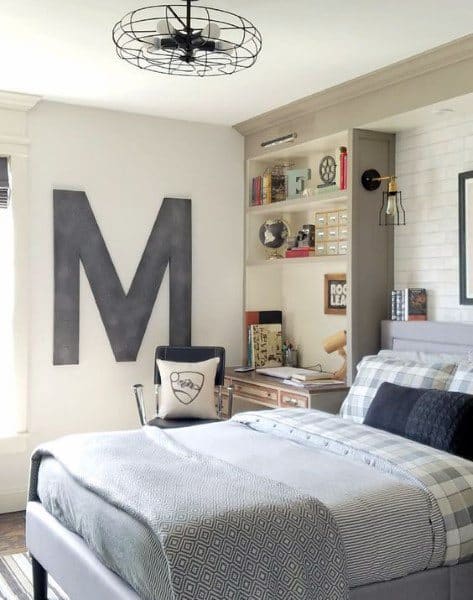 Cozy bedroom with a large letter "M" on the wall, a neatly made bed, and a desk with shelves filled with books
