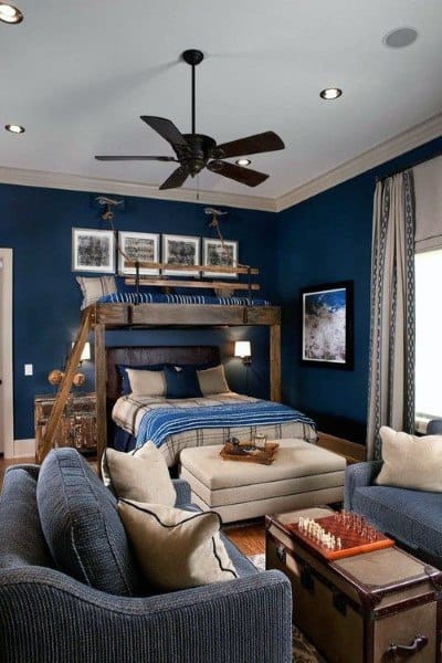 Cozy room with a loft bed, dark blue walls, ceiling fan, couch, and chess set on an ottoman