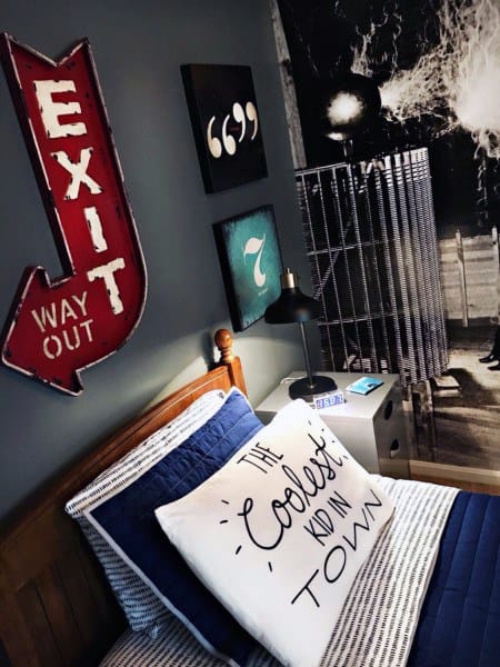 A stylish bedroom with a retro exit sign, decorative pillows, and a wall mural