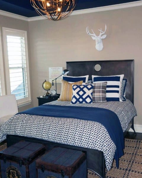 Modern bedroom with blue accents, globe decor, and deer head wall art above bed; two storage trunks at foot of bed