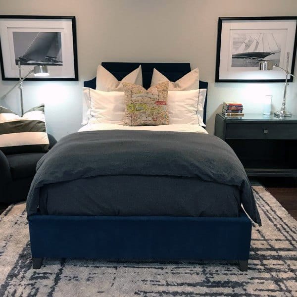 Modern bedroom with a dark blue bed, white and gray pillows, side tables, and framed sailboat photos on the wall