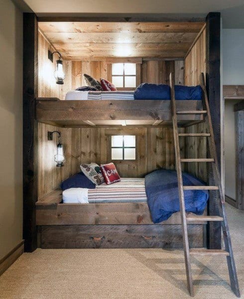 Cozy wooden bunk beds with small windows, bunk blue blankets, and decorative pillows under warm lighting