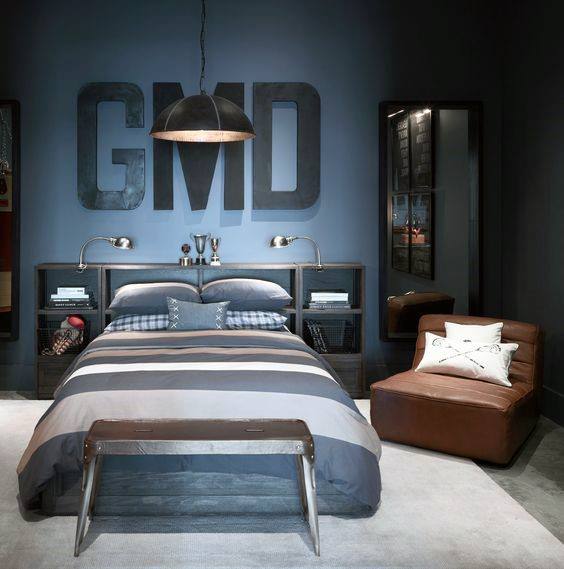 Modern bedroom with grey walls, bed with striped bedding, large wall letters "GMD," and a brown leather chair