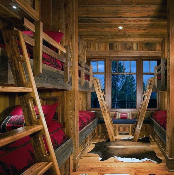 Rustic wooden bunk beds with red plaid bedding, a cowhide rug, and a window seat overlooking a forest view