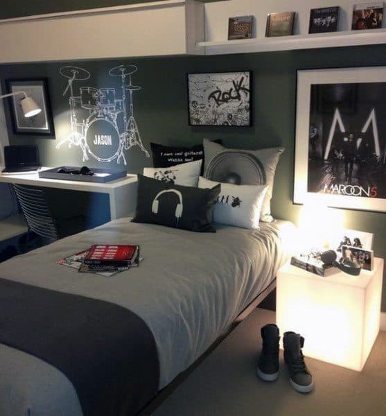 A music-themed bedroom with a bed, desk, posters, and decorative pillows; shoes and a lamp are near the bed