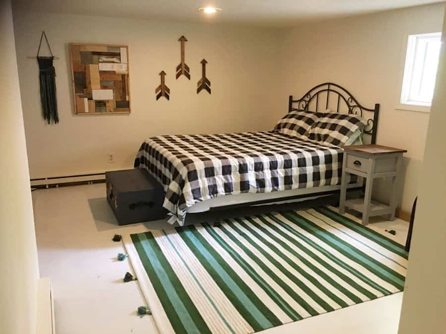 Spacious bedroom with plaid bedding, wall art, green striped rug, and metal bed frame.