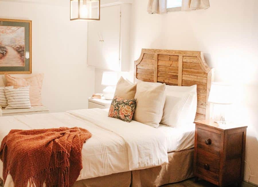 Rustic basement bedroom with wooden headboard, cozy bedding, and warm lighting.