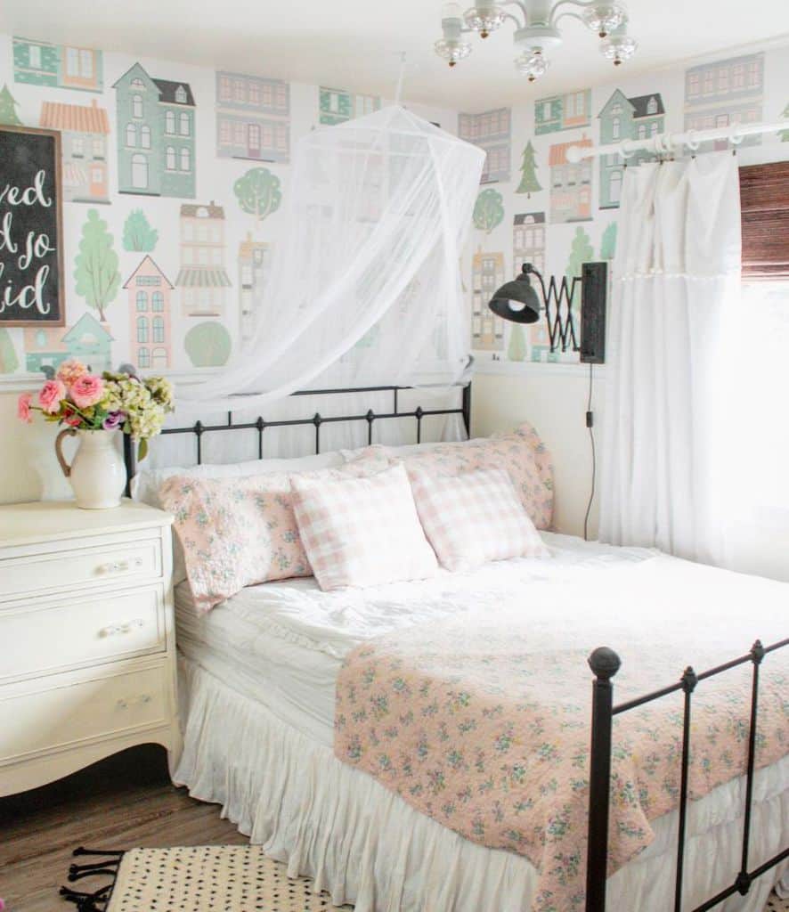 Cozy bedroom with a floral bedspread, pastel house-themed wallpaper, and a chandelier