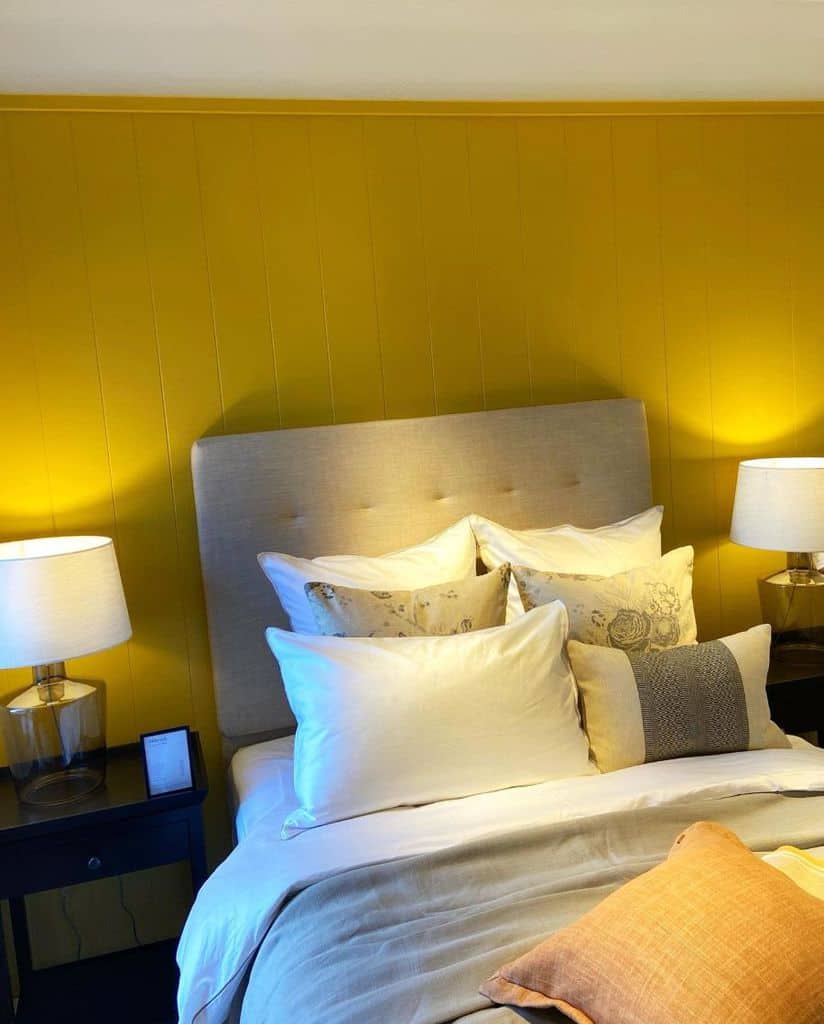 Cozy bedroom with a beige headboard, yellow wall, soft pillows, and lamps on dark nightstands